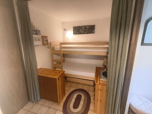 A small, cozy room with a bunk bed, a wooden nightstand, a small table, and a rug on the floor. - Apartment with ski view balcony - 4 guests (Arâches-la-Frasse)