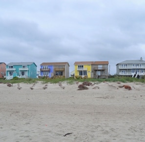 Eine Reihe von Strandhäusern mit mehreren Etagen und Balkonen, gelegen an einem sandigen Strand mit spärlicher Vegetation.