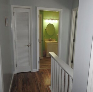 A hallway with a wooden floor leading to a bathroom with a green wall and a round mirror. - Pierfront Paradise, Oceanfront Living Next to the Pier (Atlantic Beach)
