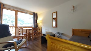 Quarto com cama, uma cadeira, uma mesa e janela com vista para uma floresta.