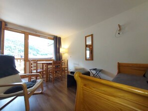 Ein Zimmer mit einem Bett, einem Sessel, einem Tisch und einem Fenster mit Blick auf einen Wald.