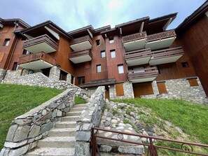 Ein mehrstöckiges Gebäude mit Holzfassade und Steindetails, mit Balkonen und einer Steintreppe, die zum Eingang führt.