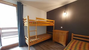 Quarto com beliche, escrivaninha e cadeira, janela com cortinas e luminária na parede.