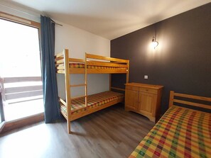 Ein Schlafraum mit Etagenbetten, einem Schreibtisch und einem Stuhl, ein Fenster mit Vorhängen und einer Wandleuchte.