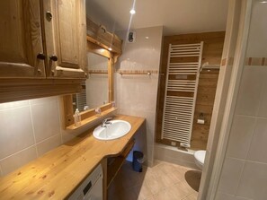 Un baño con tocador de madera, un lavabo, un espejo y una zona de ducha con puerta de madera.