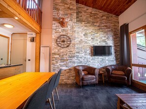 A room with a wooden ceiling, stone wall, mounted TV, leather chairs, and a wooden table. - Duplex with slope view - Valmorel - 6 guests (Valmorel)