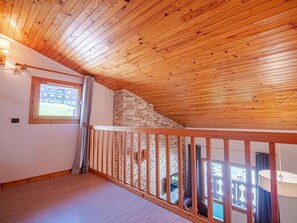 A room with a sloped wooden ceiling, a stone wall, a wooden railing, and a window with curtains. - Duplex with slope view - Valmorel - 6 guests (Valmorel)