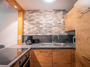 A modern kitchen with a stone backsplash, a built-in stove, a sink, and wooden cabinets. - Duplex with slope view - Valmorel - 6 guests (Valmorel)