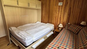 A bedroom with a bed, a wooden wardrobe, and a nightstand with a lamp. - Cozy apartment, parking - 4 guests (Les Saisies)