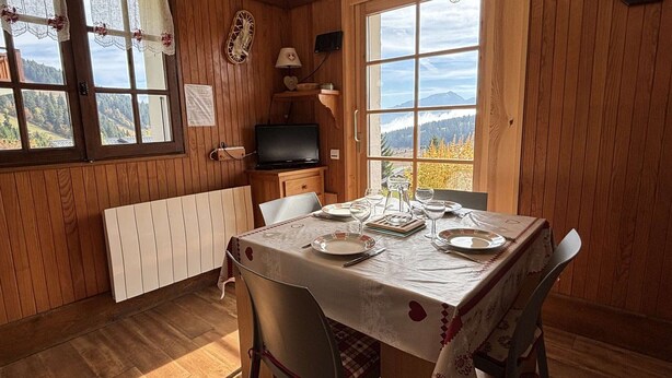 A wooden-paneled room with a dining table set for two, a television, and a view of the outdoors. - Cozy apartment, parking - 4 guests (Les Saisies)