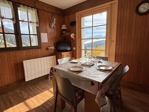 Ein Zimmer mit Holzwandverkleidung, einem Esstisch für zwei Personen, einem Fernseher und Blick ins Freie.