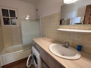 A bathroom with a bathtub, a washing machine, a sink, and a mirror. - Cozy apartment, parking - 4 guests (Les Saisies)