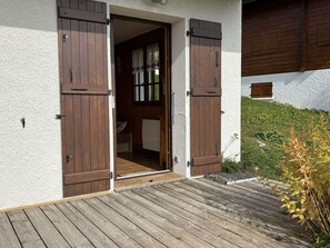 Eine Holztür mit Schiebevorrichtung, eine weiße Außenwand und ein Holzboden, der zu einem Zimmer mit Fenster und Vorhängen führt.