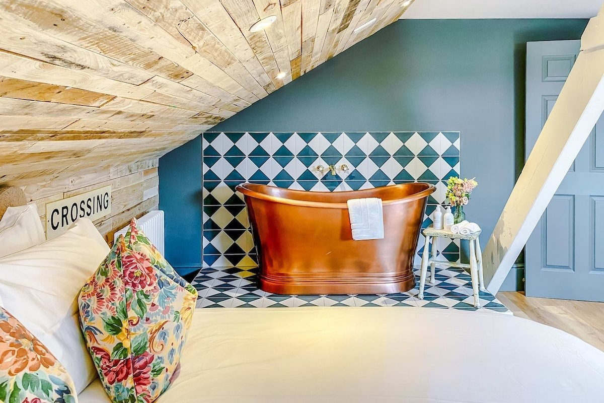 A modern bathroom with a freestanding bathtub, a tiled wall with a geometric pattern, and a wooden ceiling.