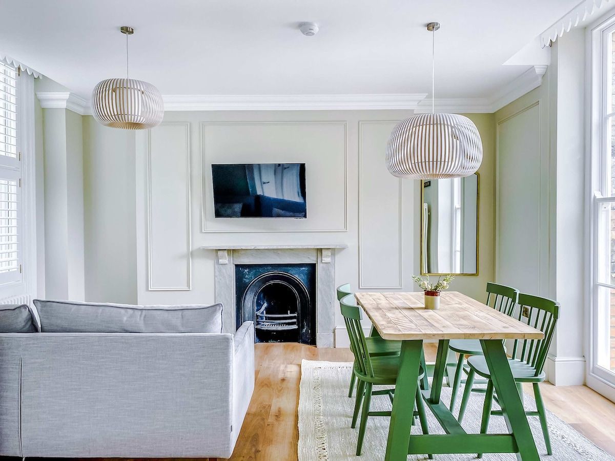 A living room with a fireplace, a dining table with chairs, a sofa, and two pendant lights.