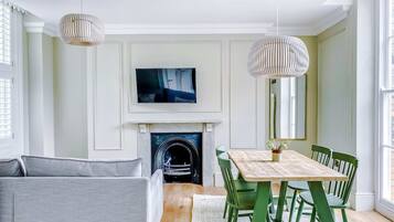 A living room with a fireplace, a dining table with chairs, a sofa, and two pendant lights.