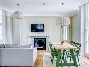 Sala de estar com lareira, mesa de jantar com cadeiras, sofá e duas luminárias pendentes.