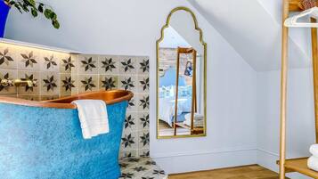 A bathroom with a blue bathtub, a mirror, and a wooden shelf.
