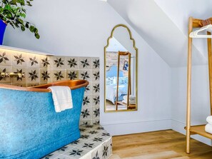 Casa de banho com banheira azul, espelho e prateleira de madeira.