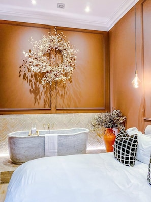 Een moderne badkamer met een vrijstaand bad, een grote spiegel en een wandlamp.