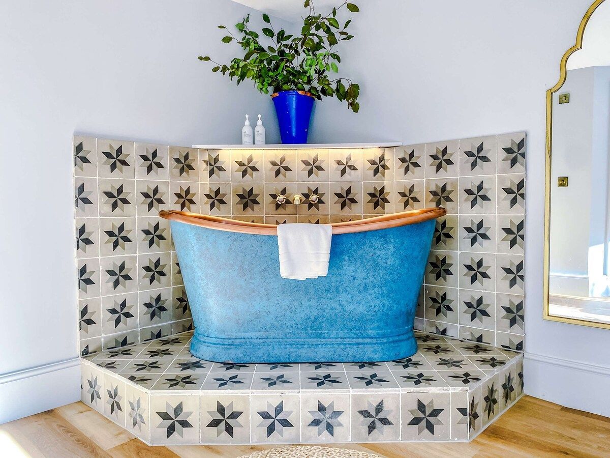 A corner bathtub with a blue finish, a white towel, and a blue planter with a plant.