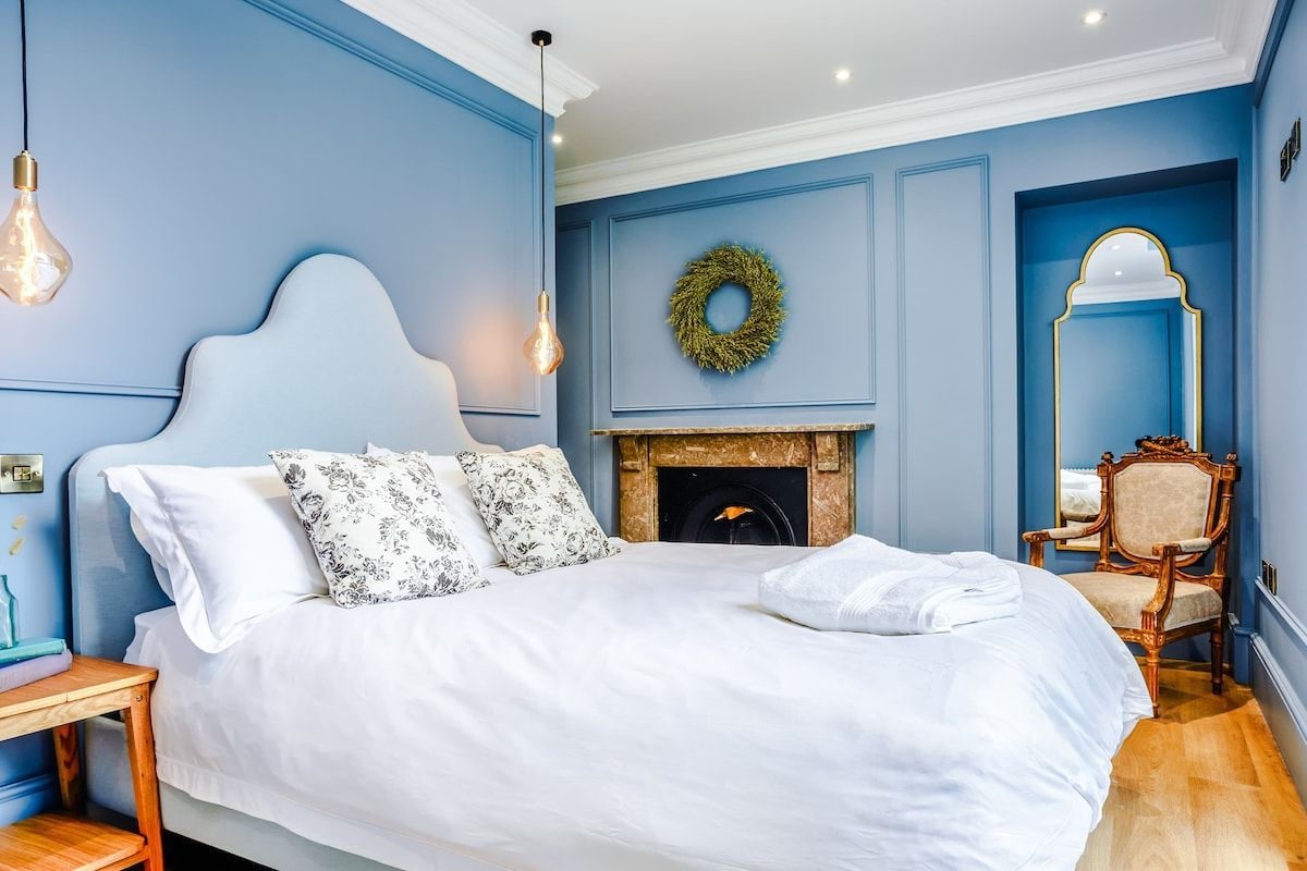 A bedroom with a large bed, a fireplace, a mirror, and a decorative wreath on the wall.