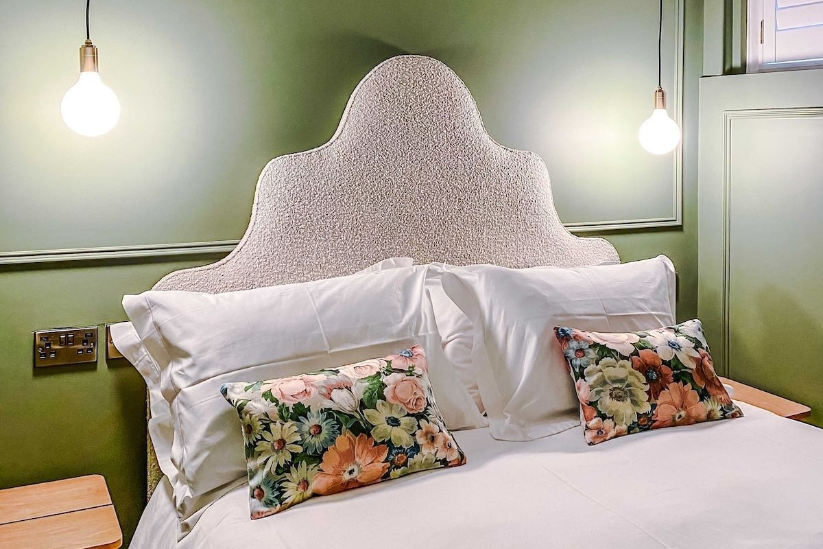 A bedroom with a bed, two pillows, a nightstand, and two hanging light fixtures.