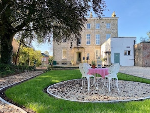 A garden with a circular seating area, a building with a stone facade, and a clear sky.