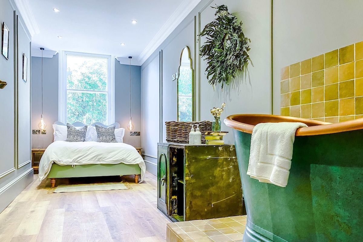 A bedroom with a bed, a green bathtub, and a window with a view of trees.