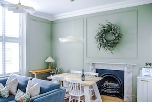 Een eethoek met een houten tafel en stoelen, een open haard en een groene krans aan de muur.