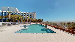 Une piscine sur le toit, avec une eau d’un bleu limpide, entourée de chaises longues et de parasols, offrant une vue sur l’océan et un bâtiment d’hôtel en arrière-plan.