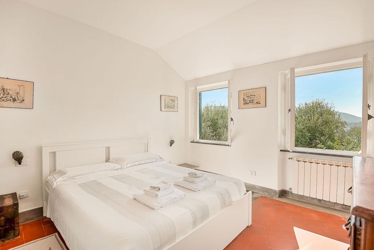 A bedroom with a large bed, two windows, and a view of greenery.
