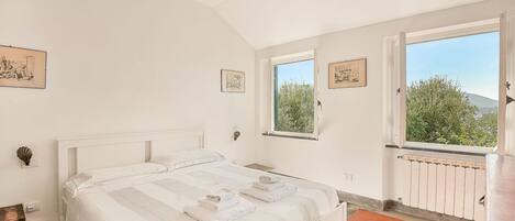 A bedroom with a large bed, two windows, and a view of greenery.