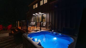Ein Whirlpool vor einem Haus mit einer Terrasse und roten Stühlen.