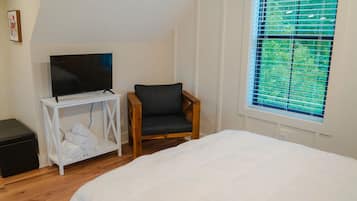 Ein Schlafzimmer mit einem Bett, einem Fernseher auf einem weißen Schrank, einem Holzstuhl und einem Fenster mit Jalousien.