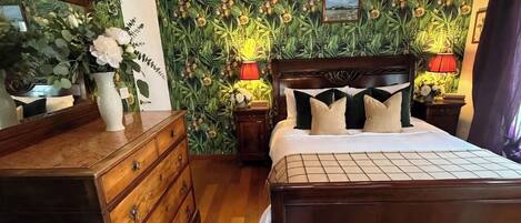 A bedroom with a wooden bed, a dresser, a mirror, and a wall with a floral wallpaper design.