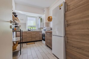 Een praktische keuken met een koelkast, fornuis, magnetron en houten keukenkastjes.