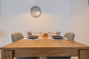 Een eettafel met vier stoelen, twee wijnglazen en een klok aan de muur.