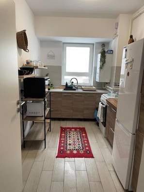 Eine kleine Küche mit Fenster, einem Kühlschrank und einer Mikrowelle.