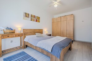 Un dormitori amb llit, taules de nit, armari, ventilador de sostre i una obra d'art penjada a la paret.