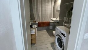 Un baño pequeño con lavadora, ducha e inodoro.
