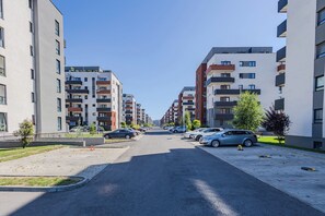 Een straat met moderne appartementencomplexen, een parkeerplaats met auto's en een heldere lucht.