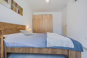 Un dormitorio con una cama de madera, un armario y un cuadro en la pared.