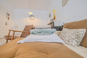 Een slaapkamer met een bruine bank, een houten stoel, een nachtkastje met een lamp en een wandklok.