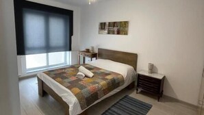 Un dormitorio con cama, ventilador de techo, ventana y mesita de noche.