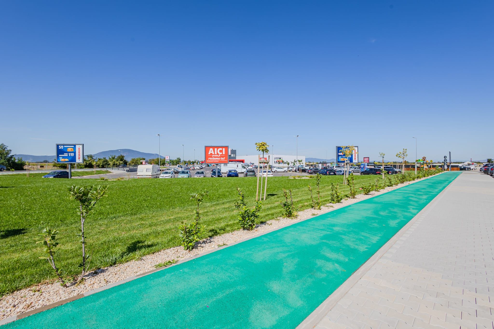 A parking lot with a green bike lane, AICI store signs, and a clear sky.