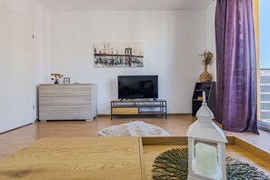 Una sala de estar moderna con una televisión de pantalla plana sobre un mueble de madera, un aparador blanco y un cuadro en la pared.