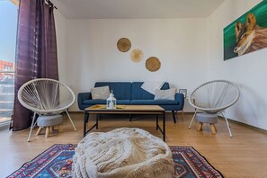 Ein modernes Wohnzimmer mit einem blauen Sofa, zwei Korbstühlen, einem Couchtisch und einem gemusterten Teppich.