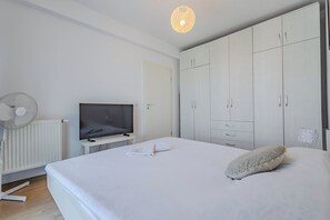 Un dormitorio con cama, televisor, armario y lámpara en el techo.