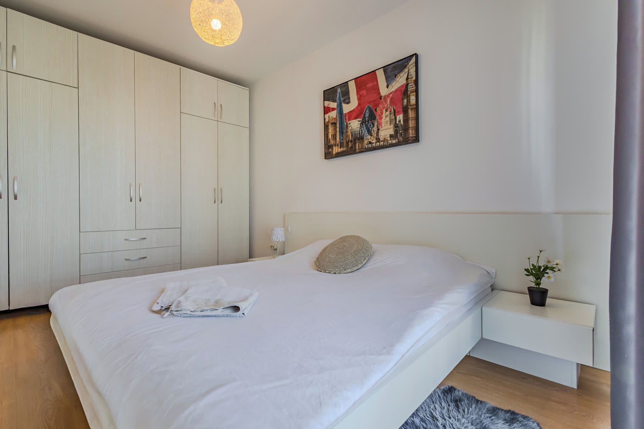 A bedroom with a large bed, a wardrobe, a bedside table with a lamp, and a painting on the wall.